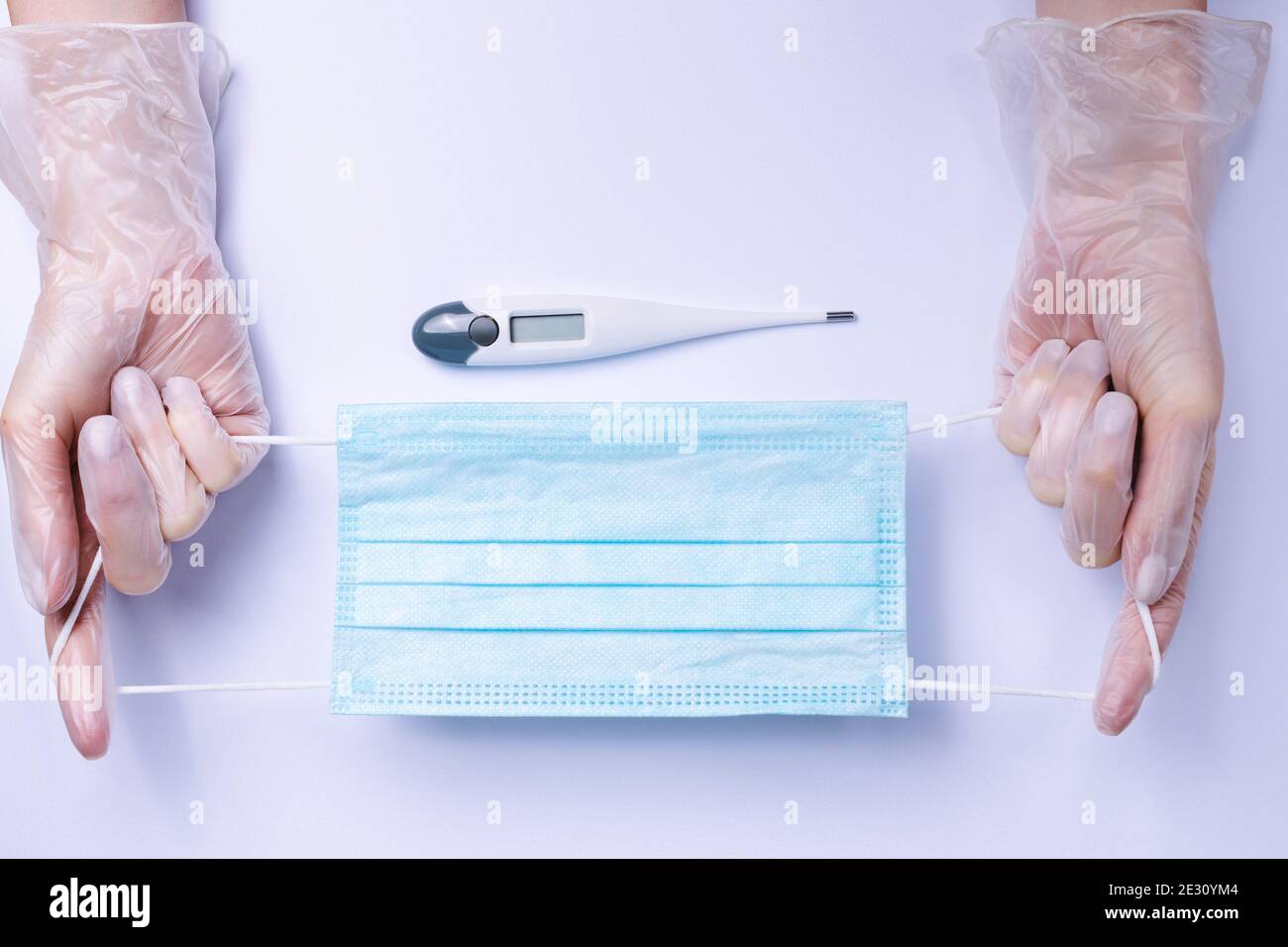 Indispensabili su sfondo bianco. Mani che allungano maschera medica e termometro. Foto Stock