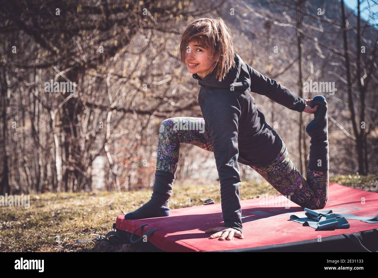 Una donna fa yoga su un tappeto di bouldering all'aperto dentro il sole Foto Stock