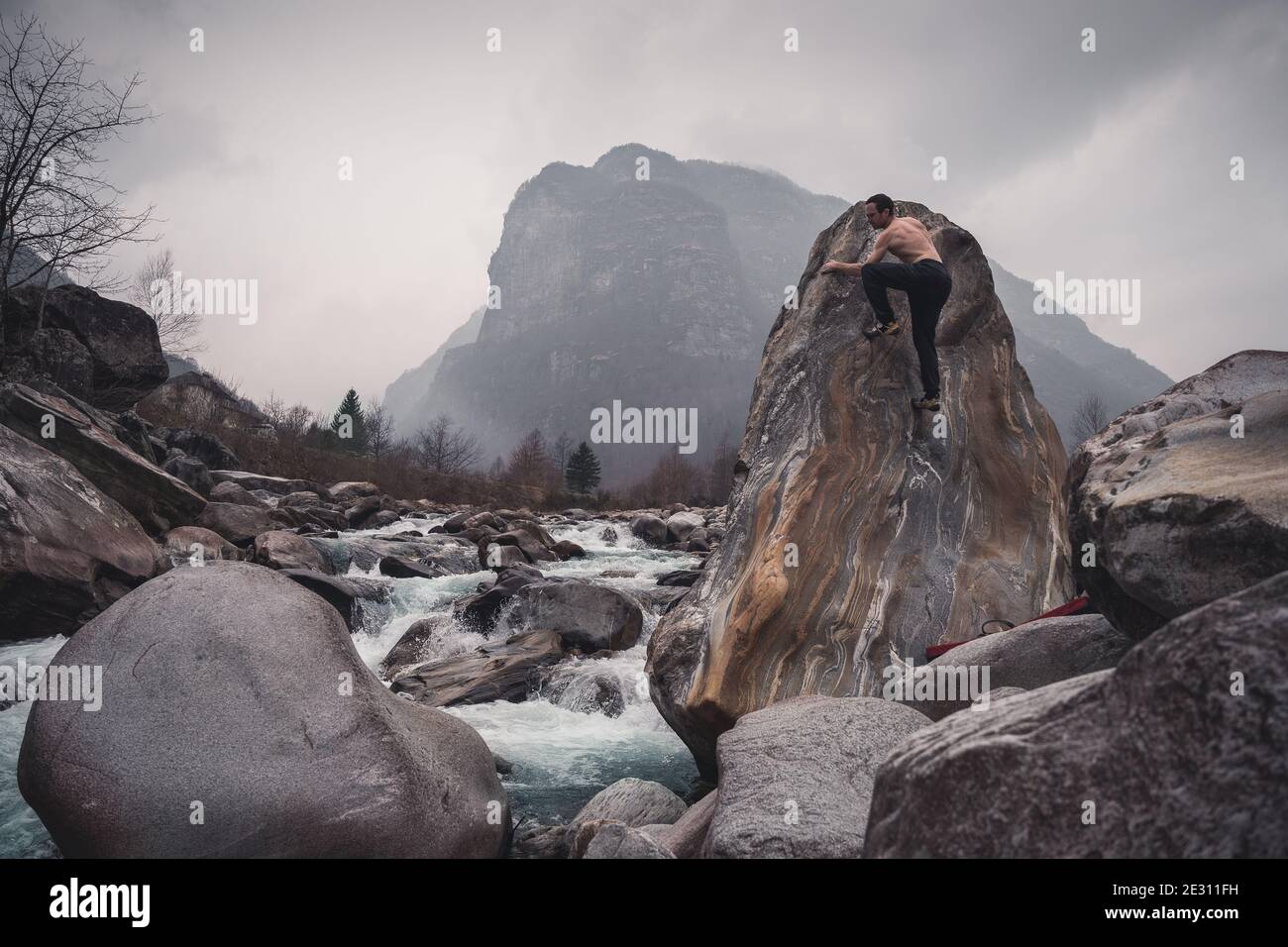 Un arrampicatore maschio su un bellissimo masso di granito lungo il fiume Verzasca nelle Alpi svizzere. Foto Stock
