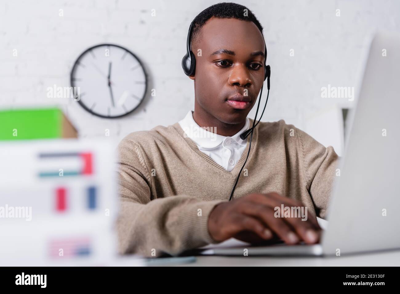giovane traduttore afroamericano in cuffia che lavora su laptop primo piano sfocato Foto Stock