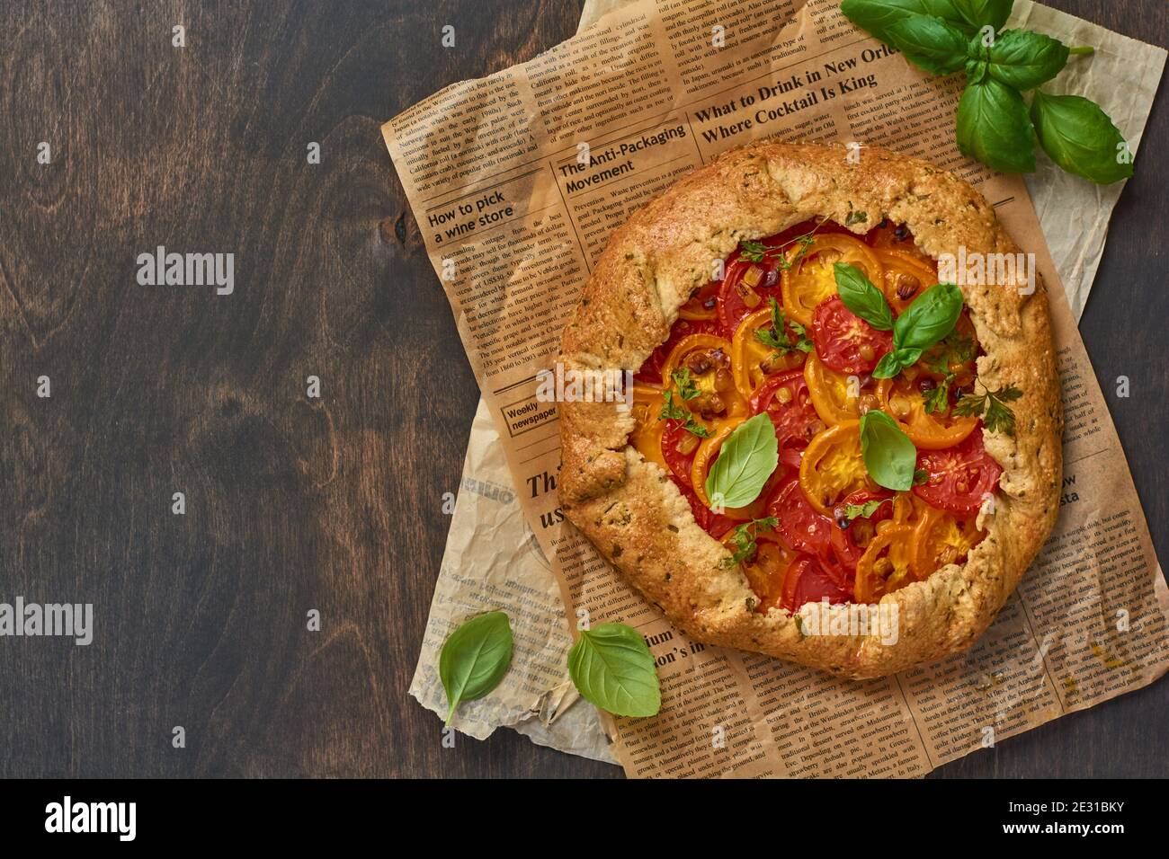 Galette o torta salata fatta in casa con pomodori rossi e gialli e basilico su vecchio giornale o carta pergamena. Foto Stock