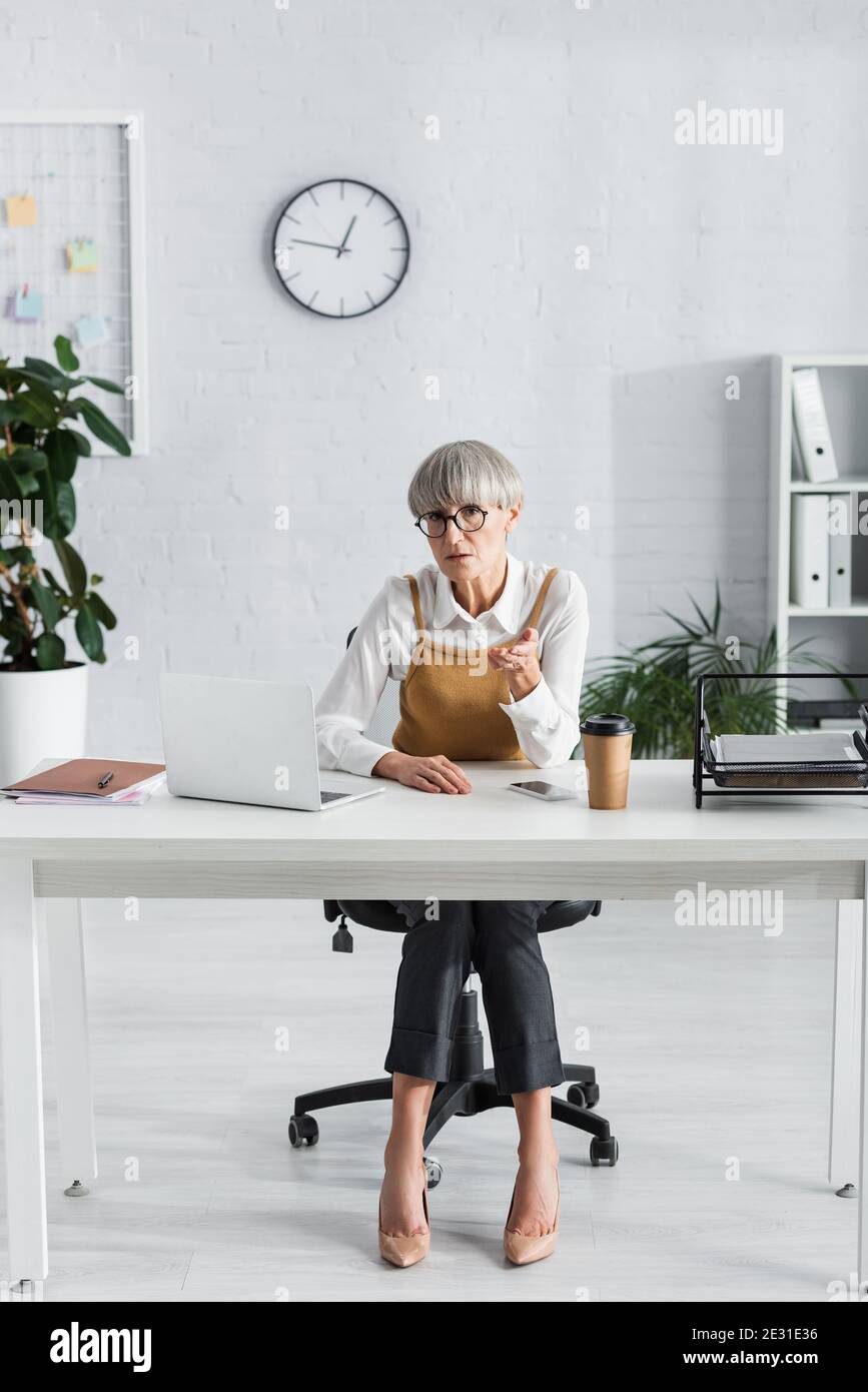 leader del team di media età in occhiali seduti alla scrivania e. puntare con la mano Foto Stock