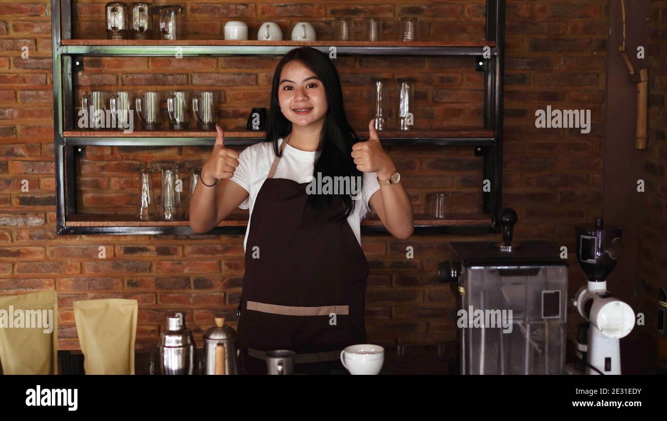 Giovane donna asiatica barista indossare grembiule OK gesto Foto Stock