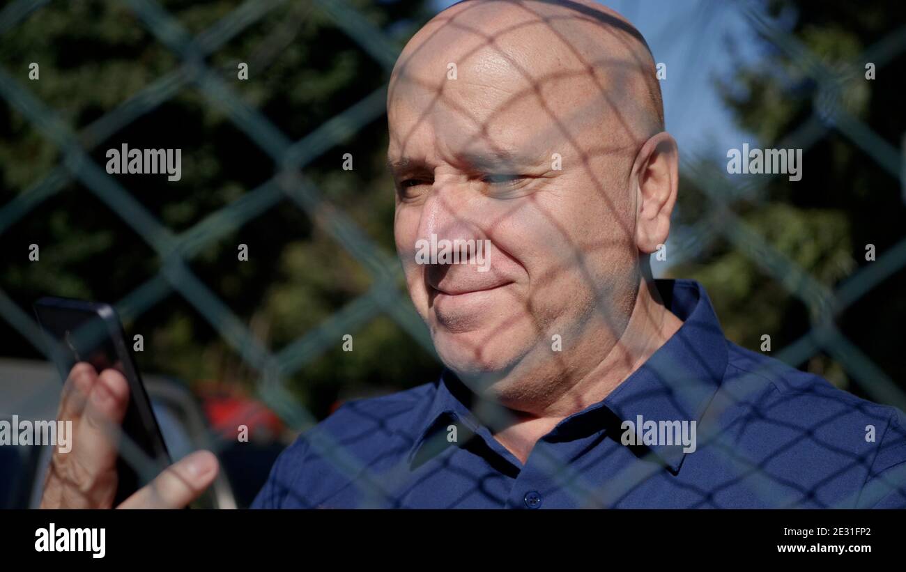 Immagine con una persona anziana dietro una recinzione metallica utilizzando Uno smartphone Foto Stock