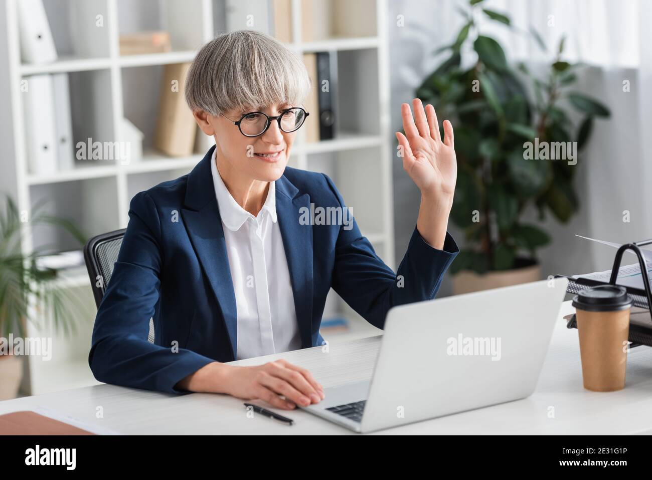 leader del team di media età in occhiali che ondolano mano durante il video chiama Foto Stock