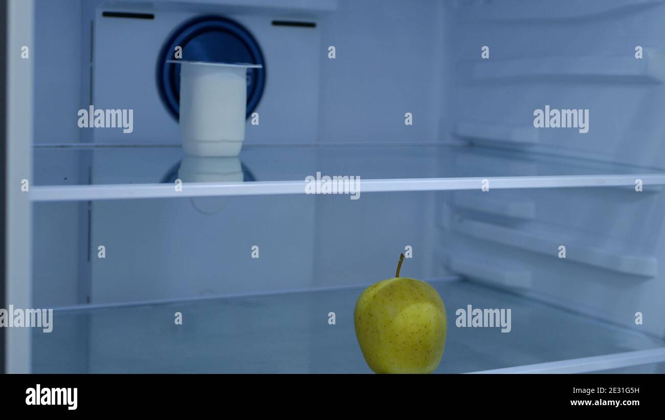 Uno yogurt freddo e una mela fresca in un vuoto Frigorifero in cucina Foto Stock