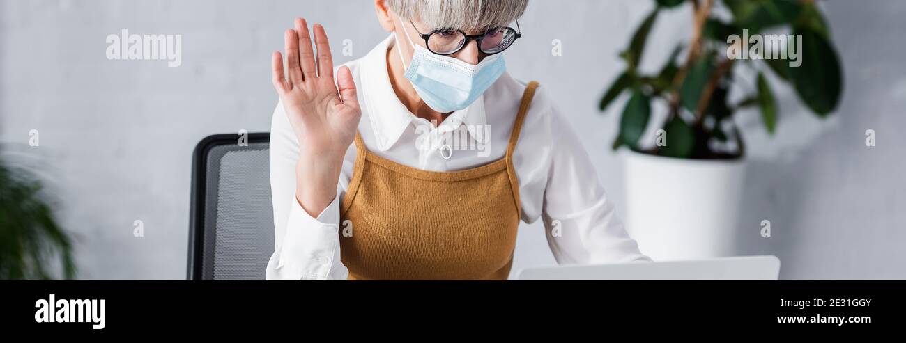 team leader di media età in occhiali e maschera medica ondeggiando mano, banner Foto Stock