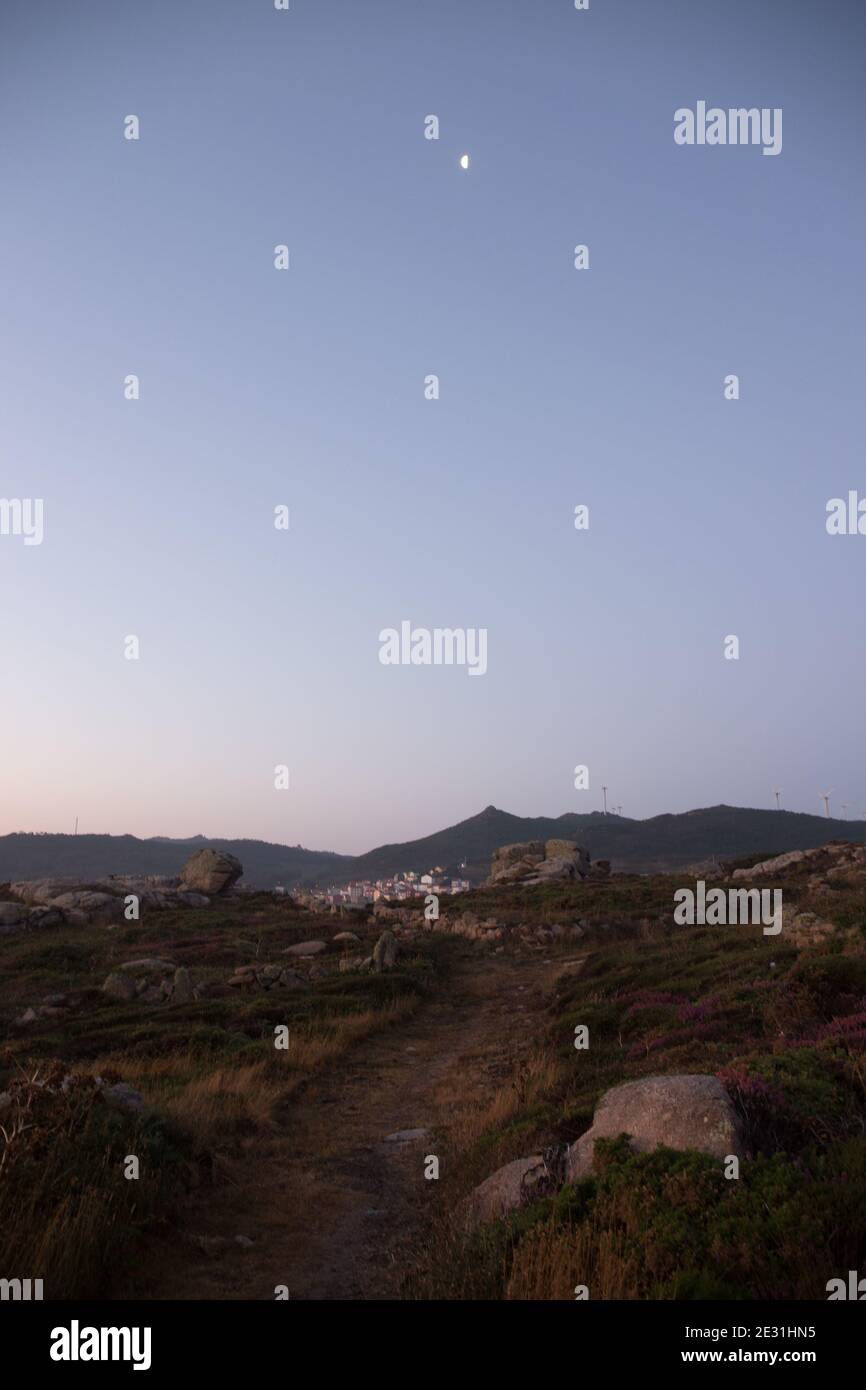 Vista del villaggio arou in lontananza al tramonto con mezza luna su un cielo limpido, la Coruña (Coruna) provincia, Galizia, Spagna Foto Stock