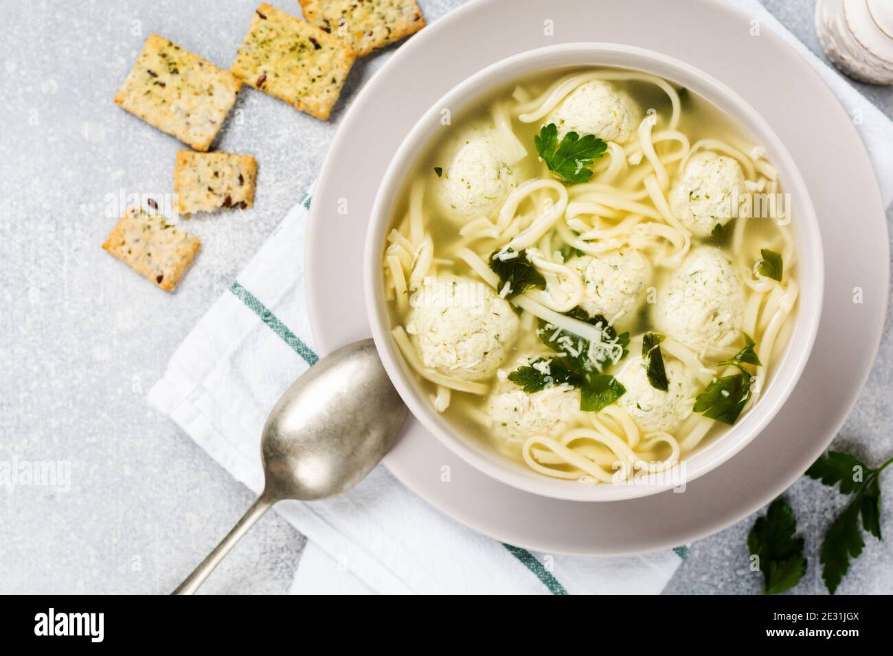 Zuppa con polpette di pollo e pasta d'uovo, parmigiano, prezzemolo in un recipiente in ceramica su uno sfondo grigio. Brodo italiano tradizionale. Vista dall'alto. Foto Stock