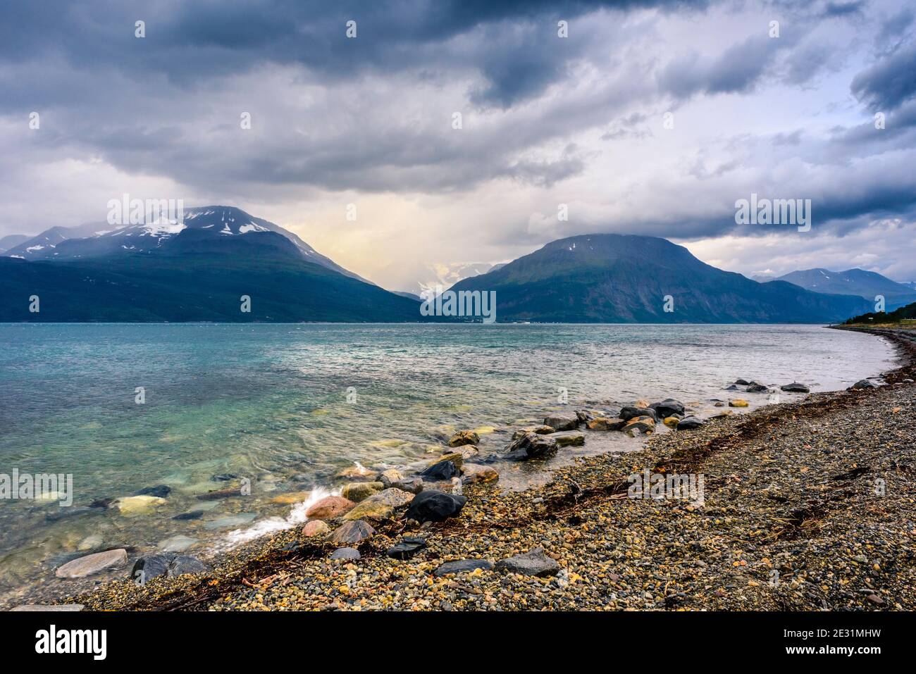 Mare turchese scintillante contro il cielo cupo con gli ultimi raggi del sole, Senja, Norvegia Foto Stock