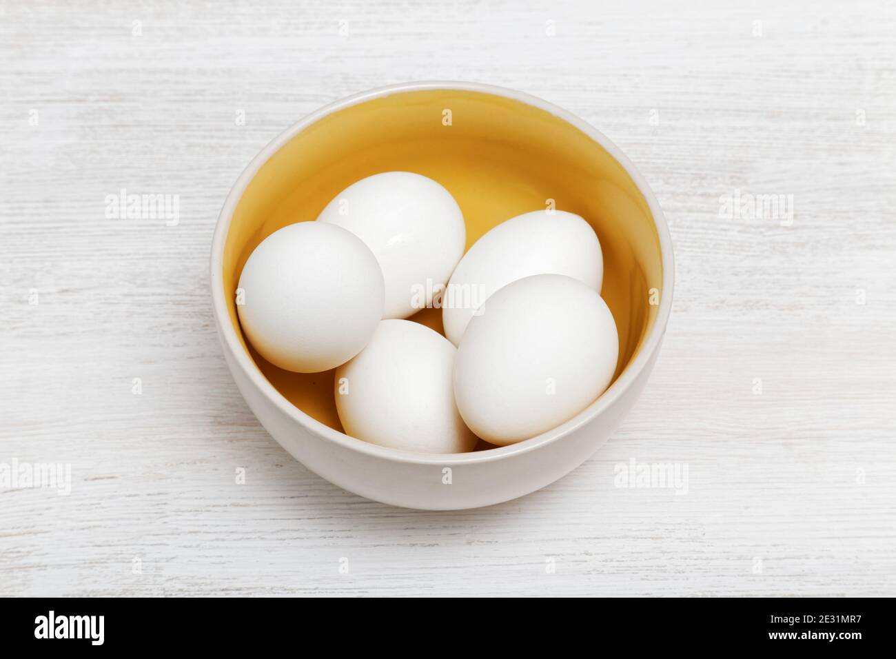 Uova di pollo bianche in un recipiente giallo e bianco tavolo di legno bianco Foto Stock