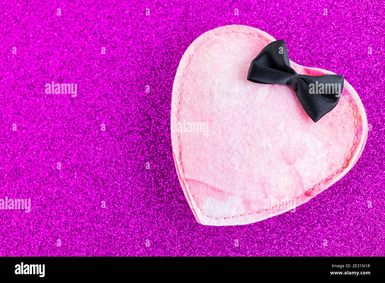 Cuore in feltro rosa su uno sfondo con glitter viola. Cuore in feltro con cravatta nera. Concetto di San Valentino. Spazio di copia. Vista dall'alto Foto Stock