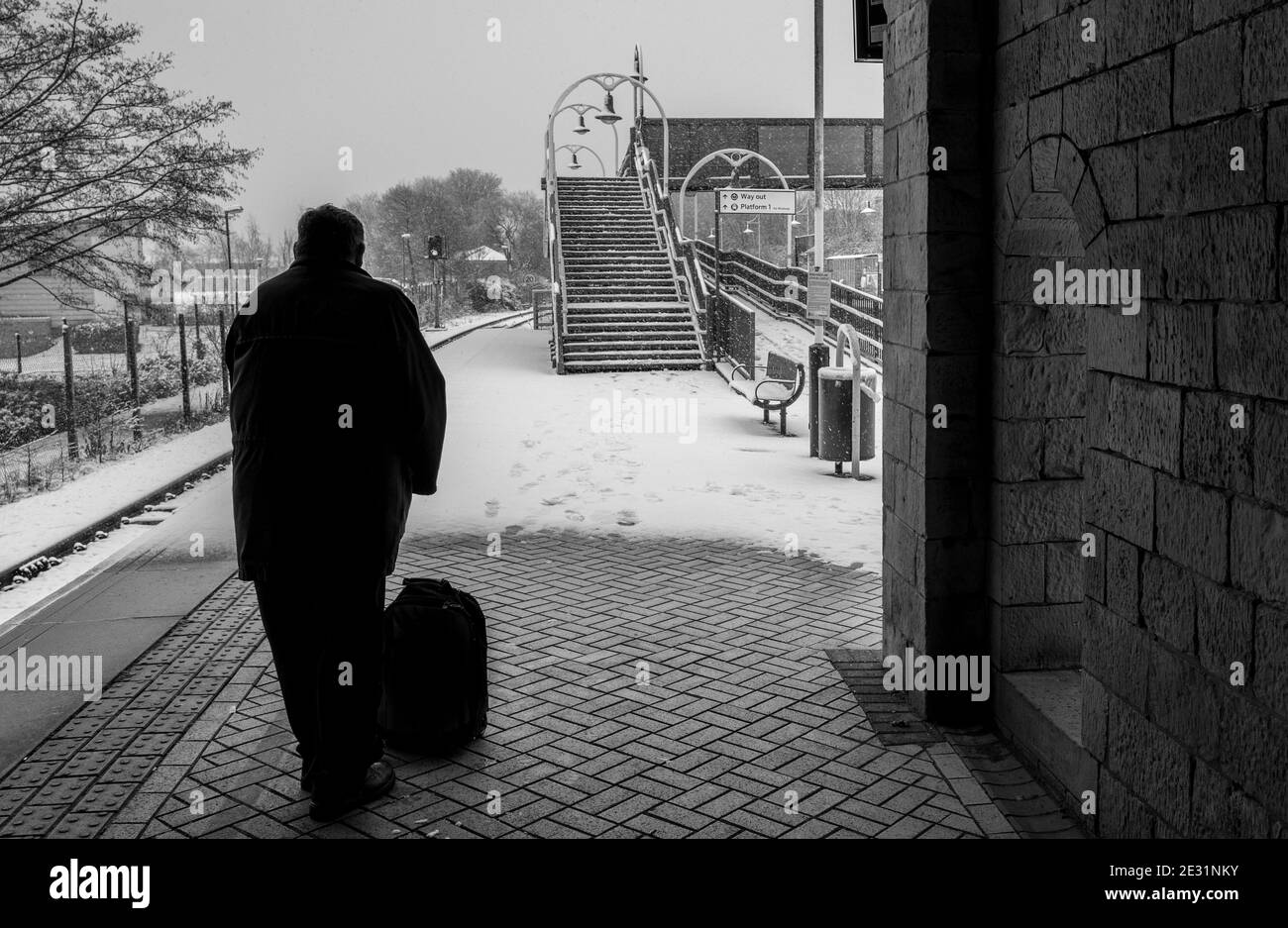 Silhoulette di un passeggero maschile al riparo dalla neve in una stazione ferroviaria locale. Foto Stock