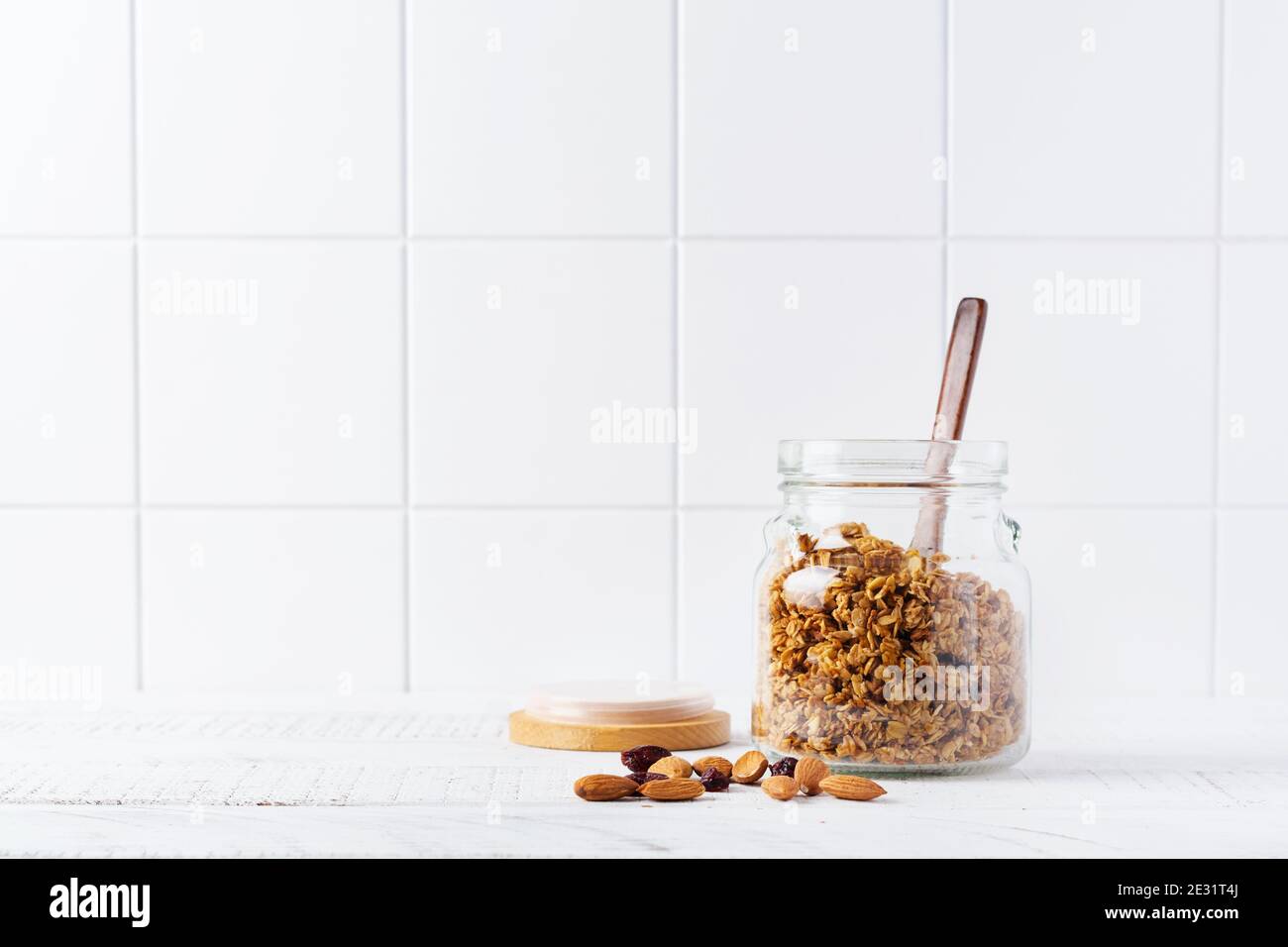 Granola di avena con noci e frutta secca per preparare una sana colazione su un luminoso tavolo da cucina. Stile bianco scandinavo. Messa a fuoco selettiva. Foto Stock