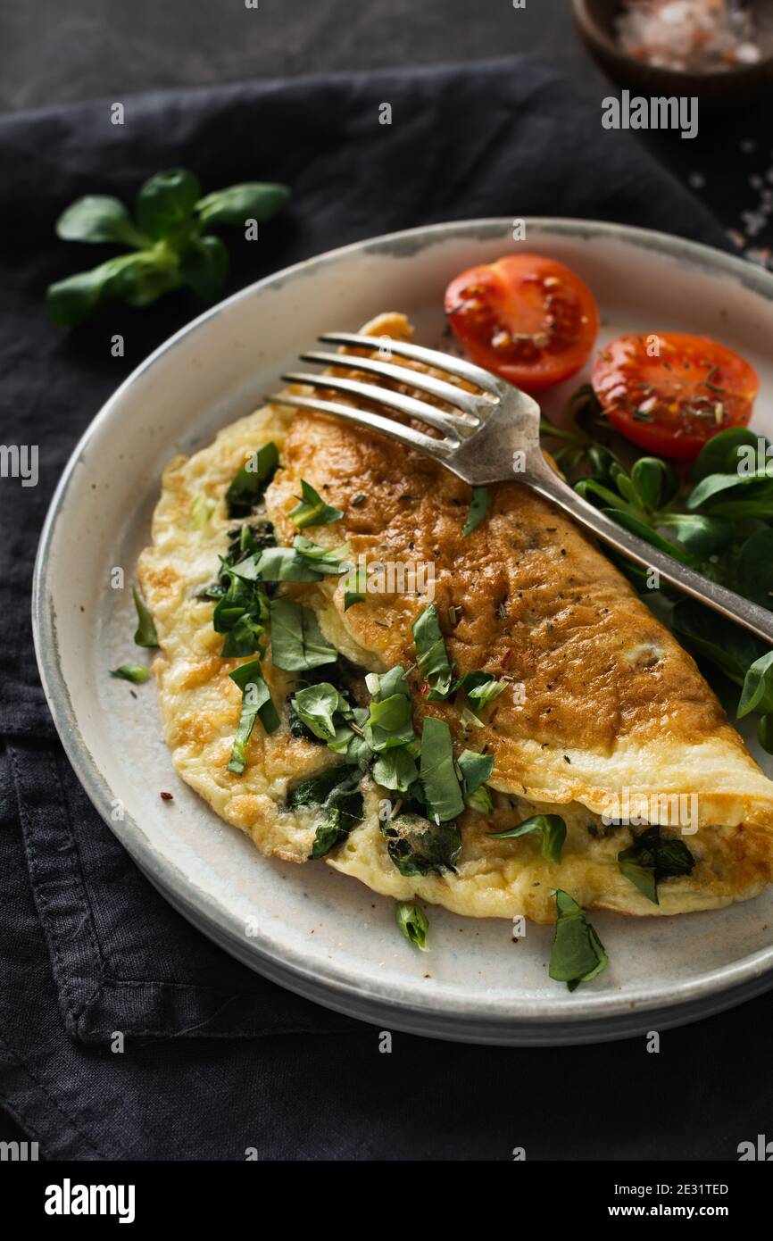 Omelette ripiena con pomodori, peperone rosso, formaggio cremoso e mais o lattuga di agnello su sfondo di legno scuro con spazio per la copia. Alimentazione sana Foto Stock