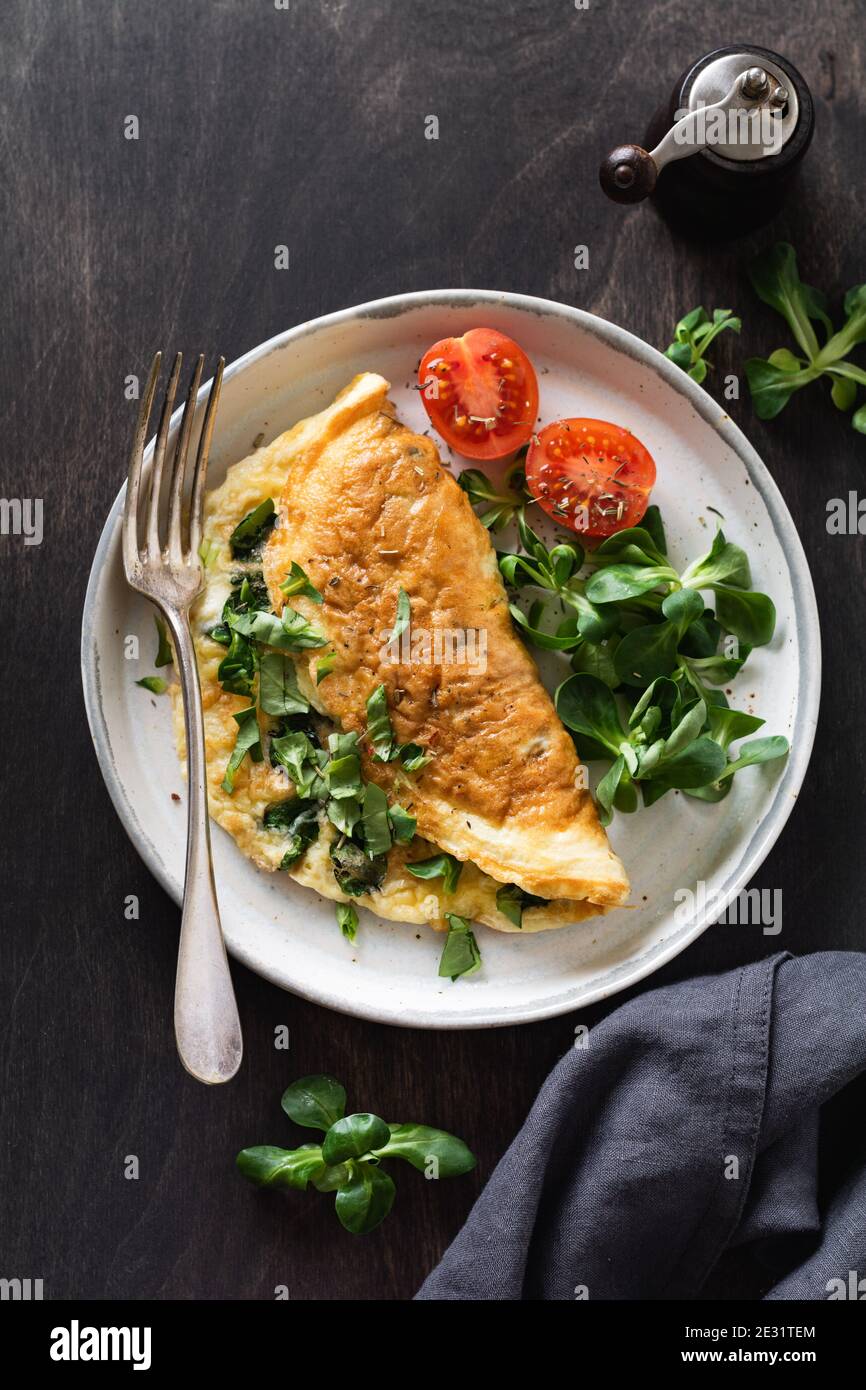 Omelette ripiena con pomodori, peperone rosso, formaggio cremoso e mais o lattuga di agnello su sfondo di legno scuro con spazio per la copia. Alimentazione sana Foto Stock