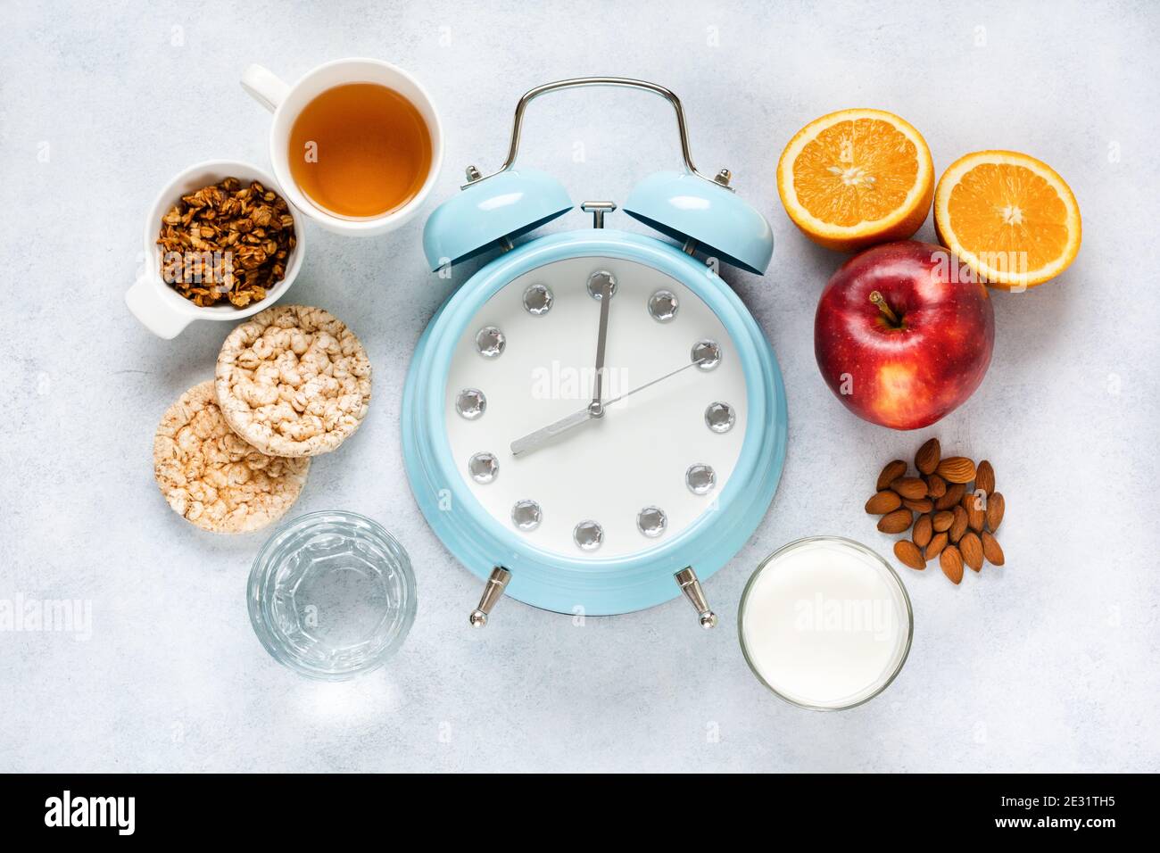 Concetto di corretta alimentazione porzionata per la salute calcolato dall'orologio. Gruppo utile prima colazione caffè, tè, frutta, avena, noci, latte, acqua, muesli. Foto Stock