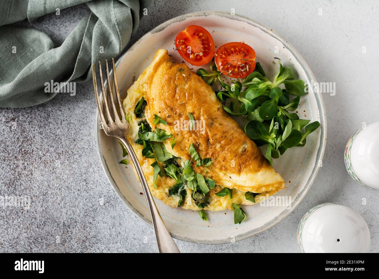 Omelette ripiena con pomodori, peperone rosso, formaggio cremoso e lattuga di mais o di agnello su fondo di cemento chiaro con spazio di copia. Dieta sana per Foto Stock