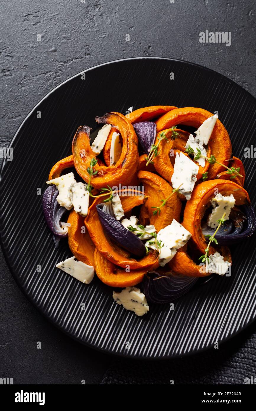 Fette di zucca al forno, cipolle, aglio, spezie e fette di formaggio Dorblu su piastra di ceramica nera e vecchio fondo di pietra nera. Vista dall'alto. Foto Stock