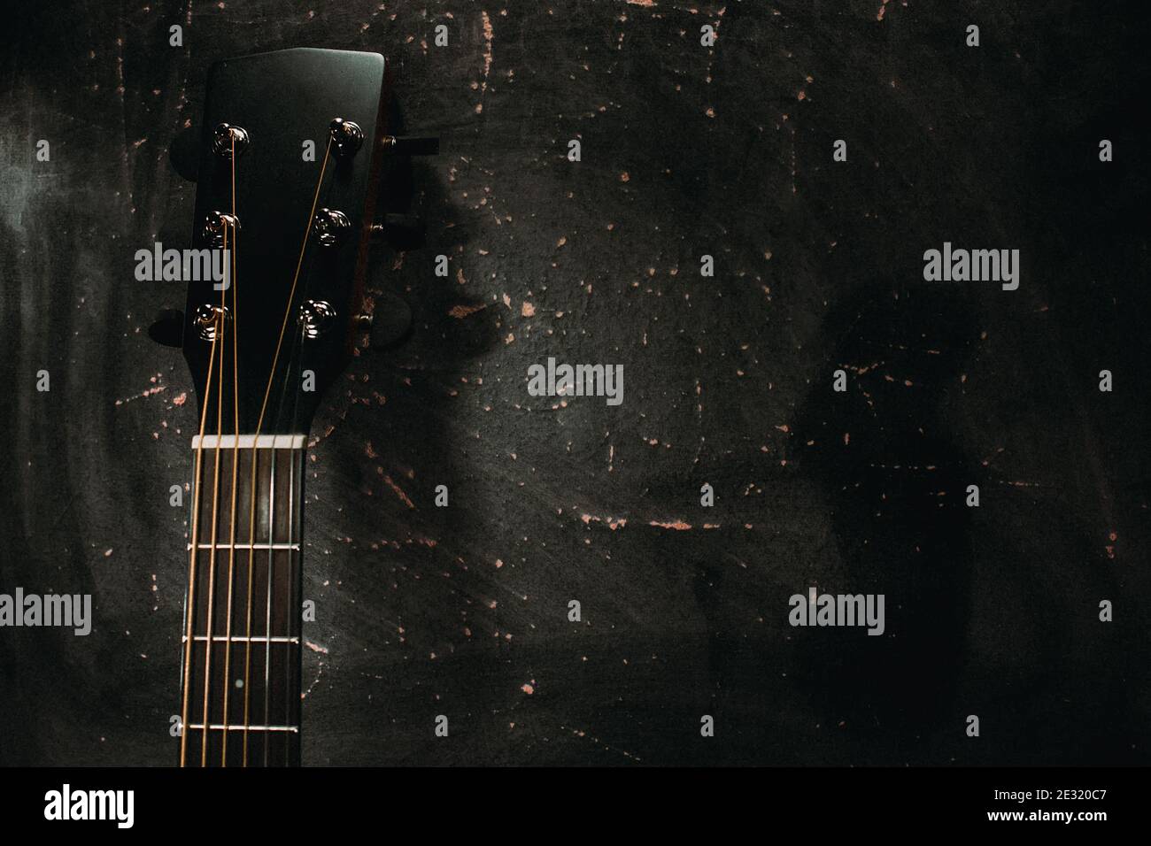 Una chitarra acustica si erge contro il muro contro uno sfondo scuro. Foto Stock