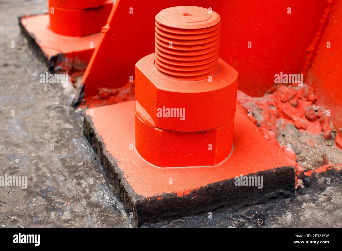 Il supporto in metallo rosso è imbullonato alla base in calcestruzzo con bulloni grandi. Fissaggio a terra di una torre o di una torre. Foto Stock
