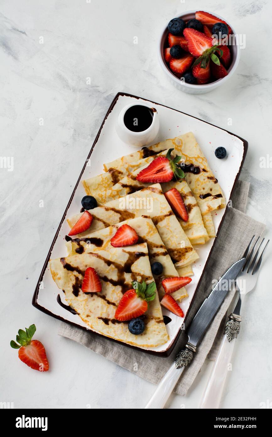 Deliziosa crepe con condimento al cioccolato e fragola fresca su piatto bianco, vista dall'alto. Foto Stock