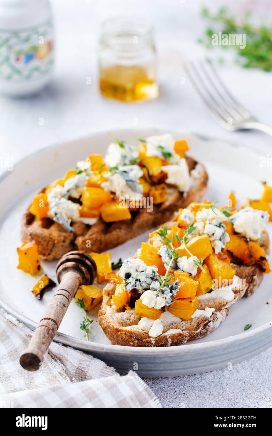 Panino di zucca al forno con formaggio dorblu con muffa blu, miele e timo su un fondo di cemento vecchio chiaro. Vista dall'alto. Foto Stock