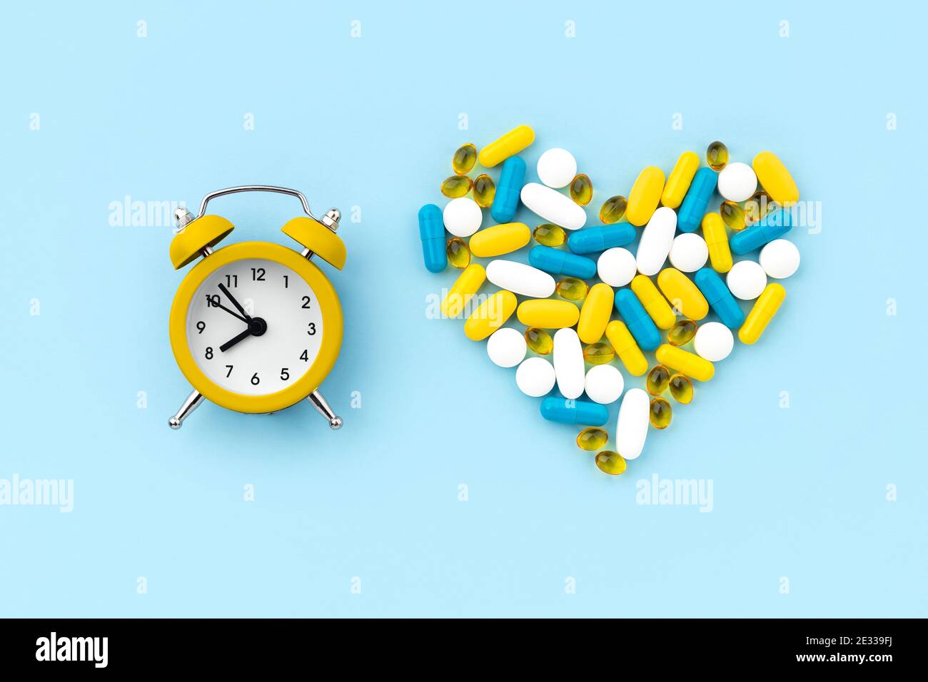 Pillole mediche a forma di cuore con sveglia su blu sfondo Foto Stock