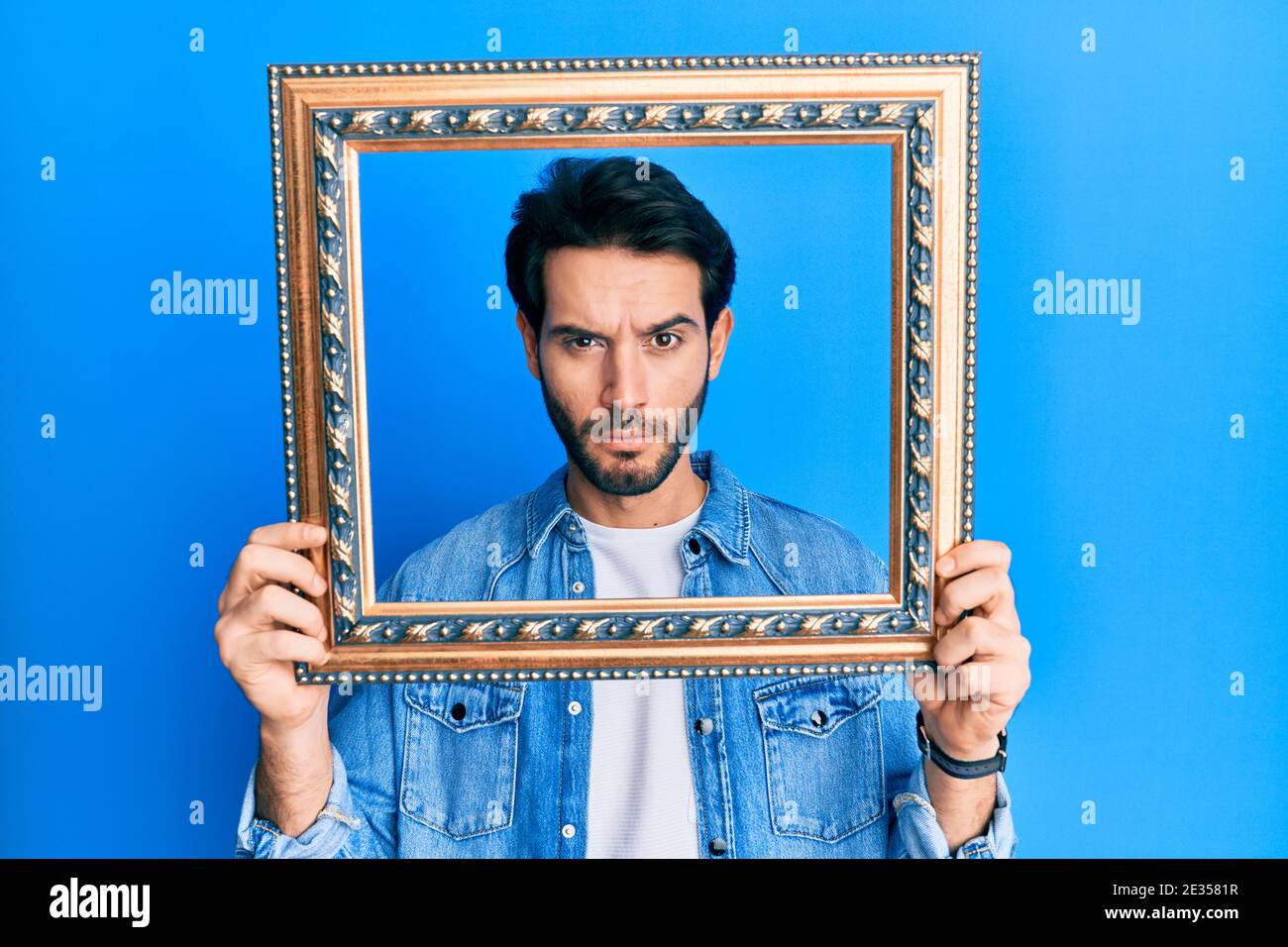 Giovane uomo ispanico che tiene a telaio vuoto scettico e nervoso, accigliato sconvolto a causa del problema. Persona negativa. Foto Stock