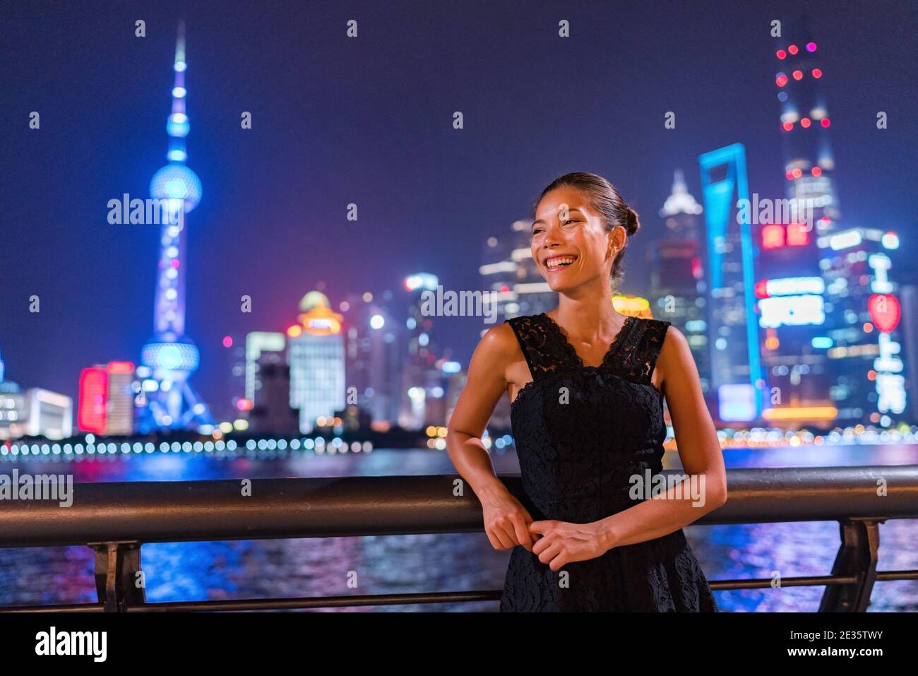 Elegante donna asiatica sorridente godendo il night club uscendo dentro Abito nero di moda vicino al fiume Bund in vista di Shanghai Delle luci della città dello skyline di Pudong Foto Stock