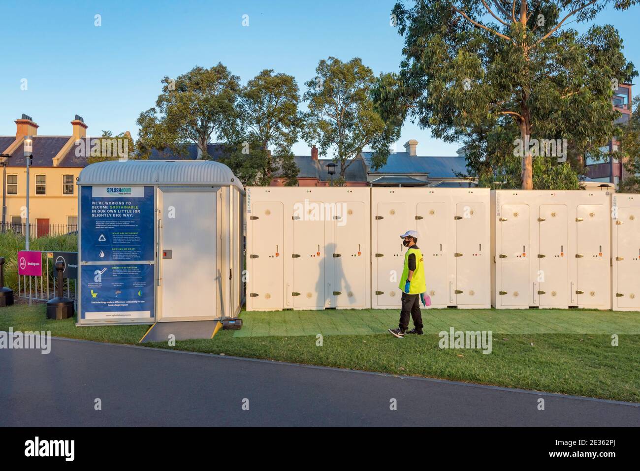 Un pulitore che indossa una maschera Covid si trova di fronte a un bagno portatile con accesso per disabili e a una fila di singoli servizi igienici portatili in occasione di un evento del Festival di Sydney. Foto Stock