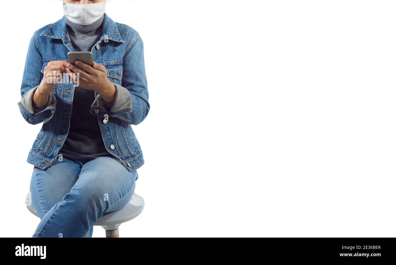 Un turista in maschera medica siede sul thechair e utilizzando il telefono cellulare isolato su sfondo bianco.Travel e concetto di coronavirus. Foto Stock
