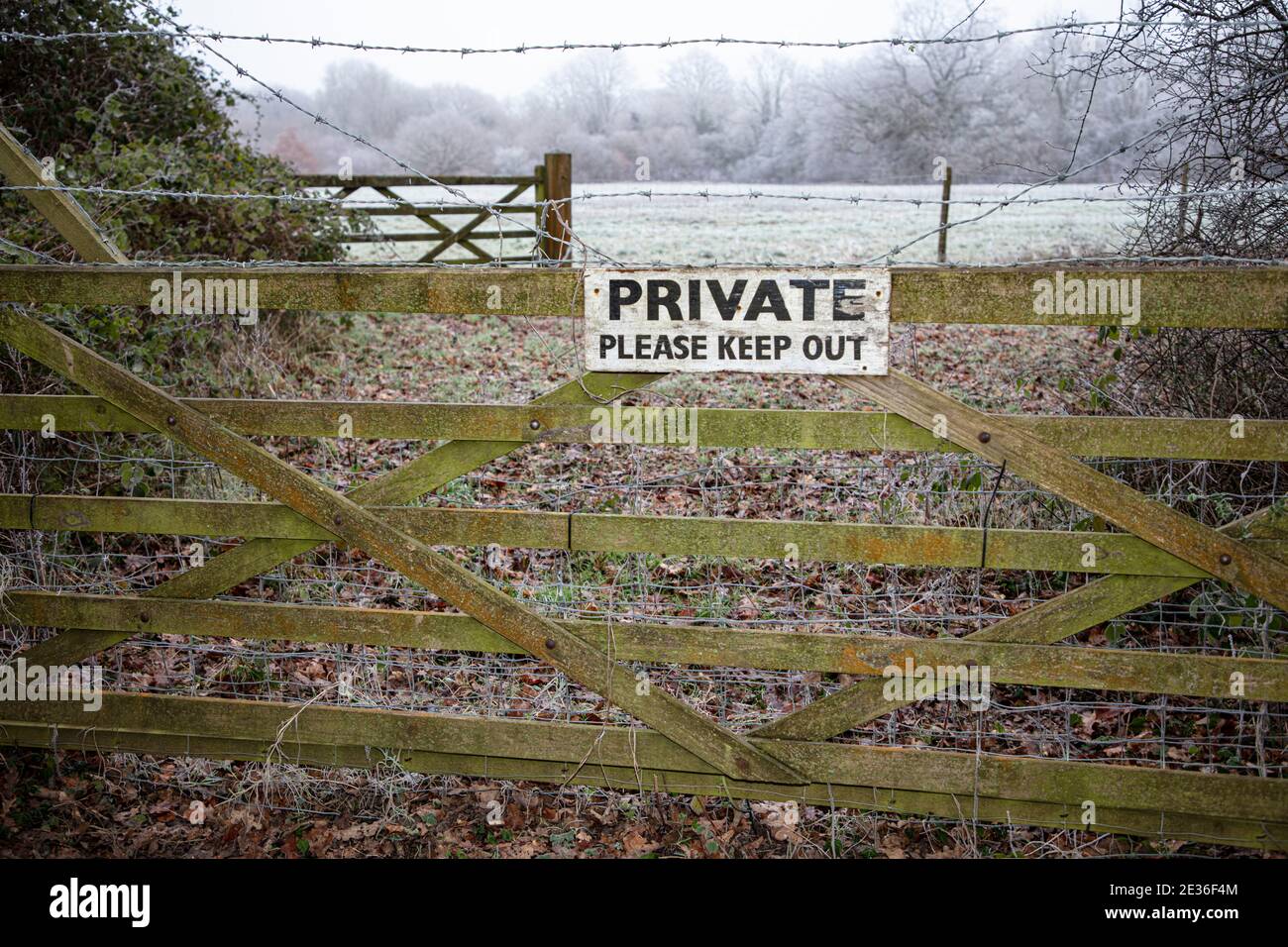 Un cartello "privato da tenere fuori" su un cancello invernale gelido con filo spinato Foto Stock