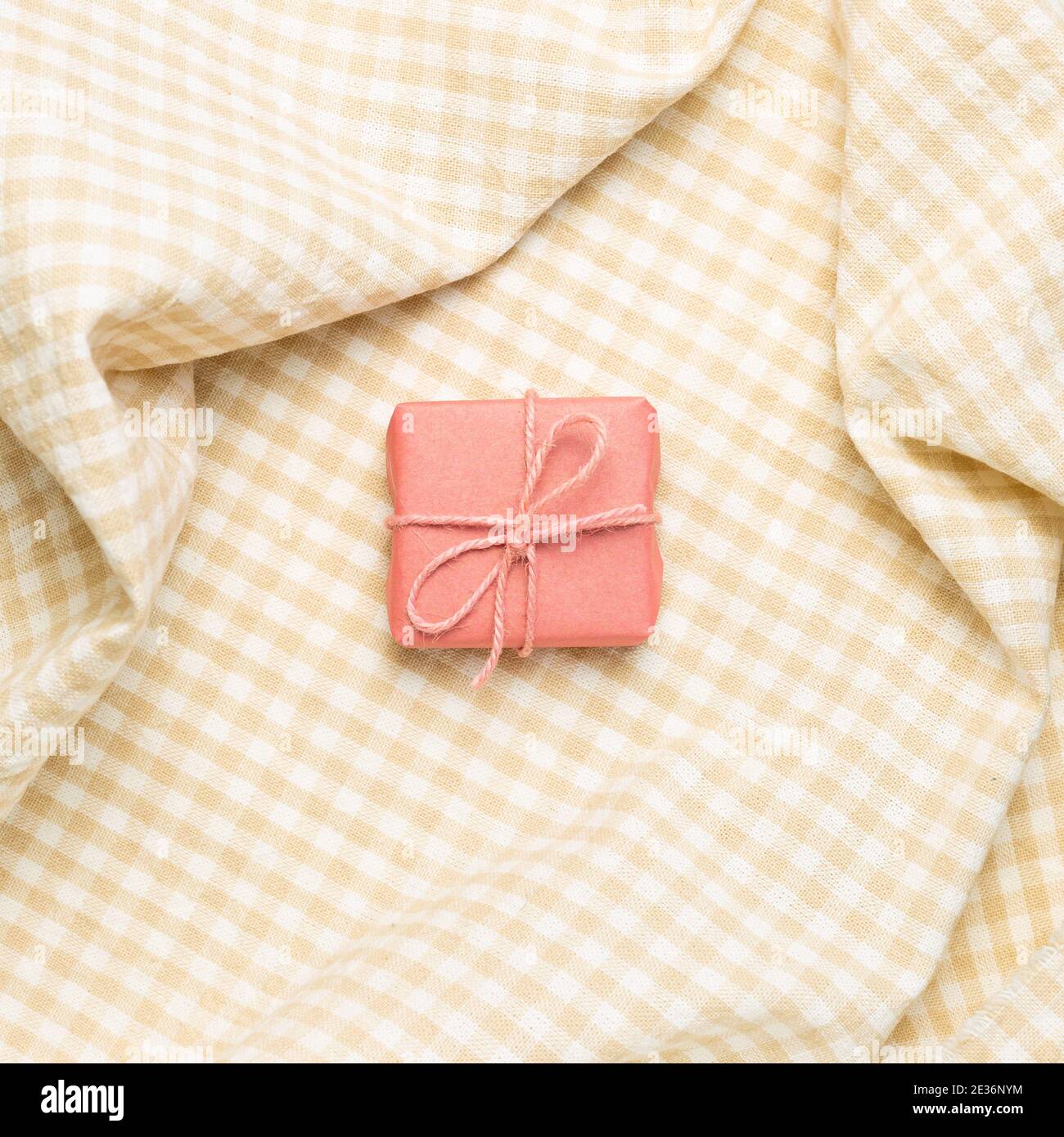 Confezione regalo rosa su fondo in tessuto di controllo beige sminuzzato. Vista dall'alto Foto Stock