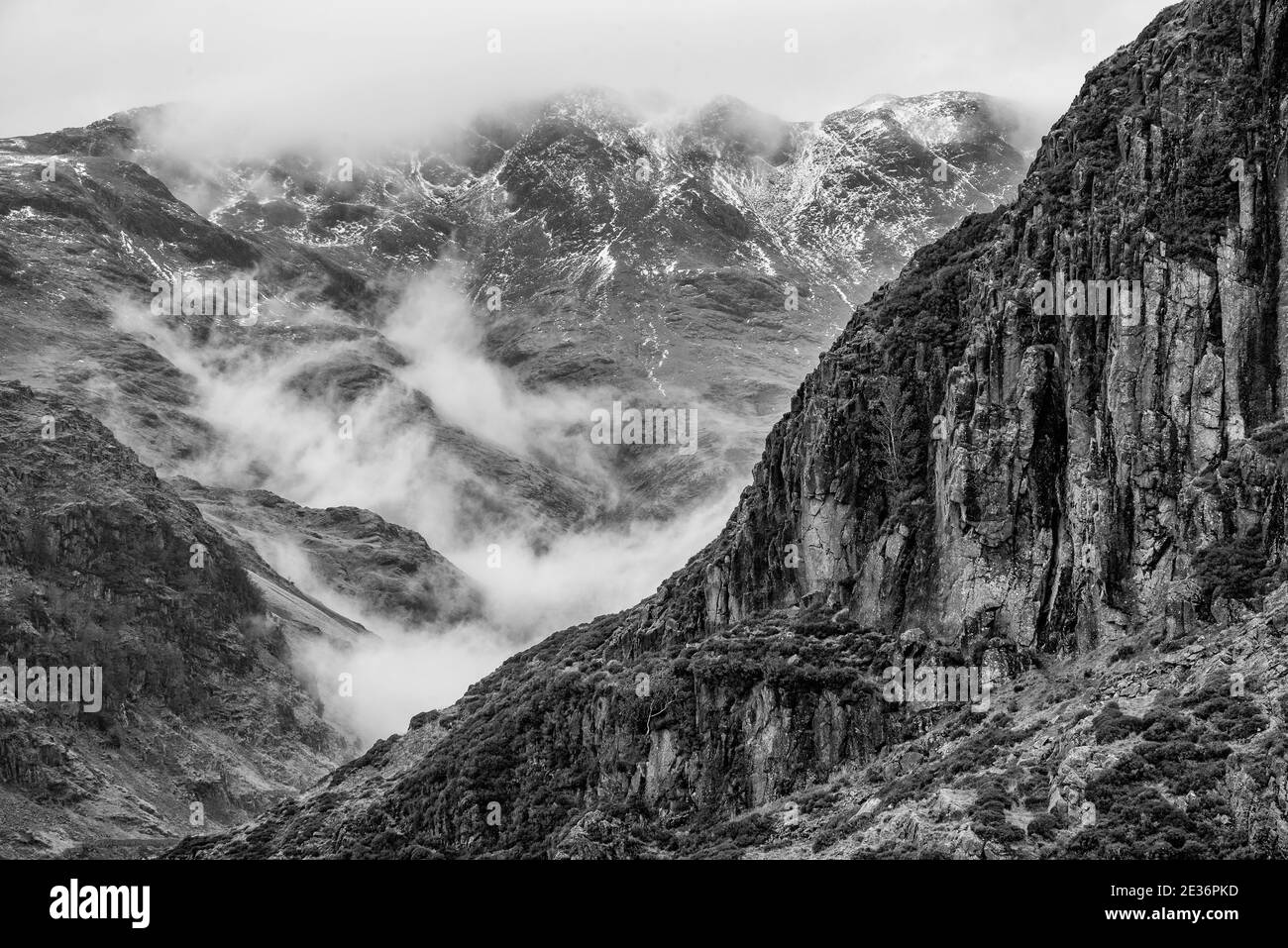 Splendida immagine in bianco e nero del paesaggio invernale Side Pike verso Langdale Pikes con le nuvole di basso livello su cime di montagna e nebbia di moody Foto Stock
