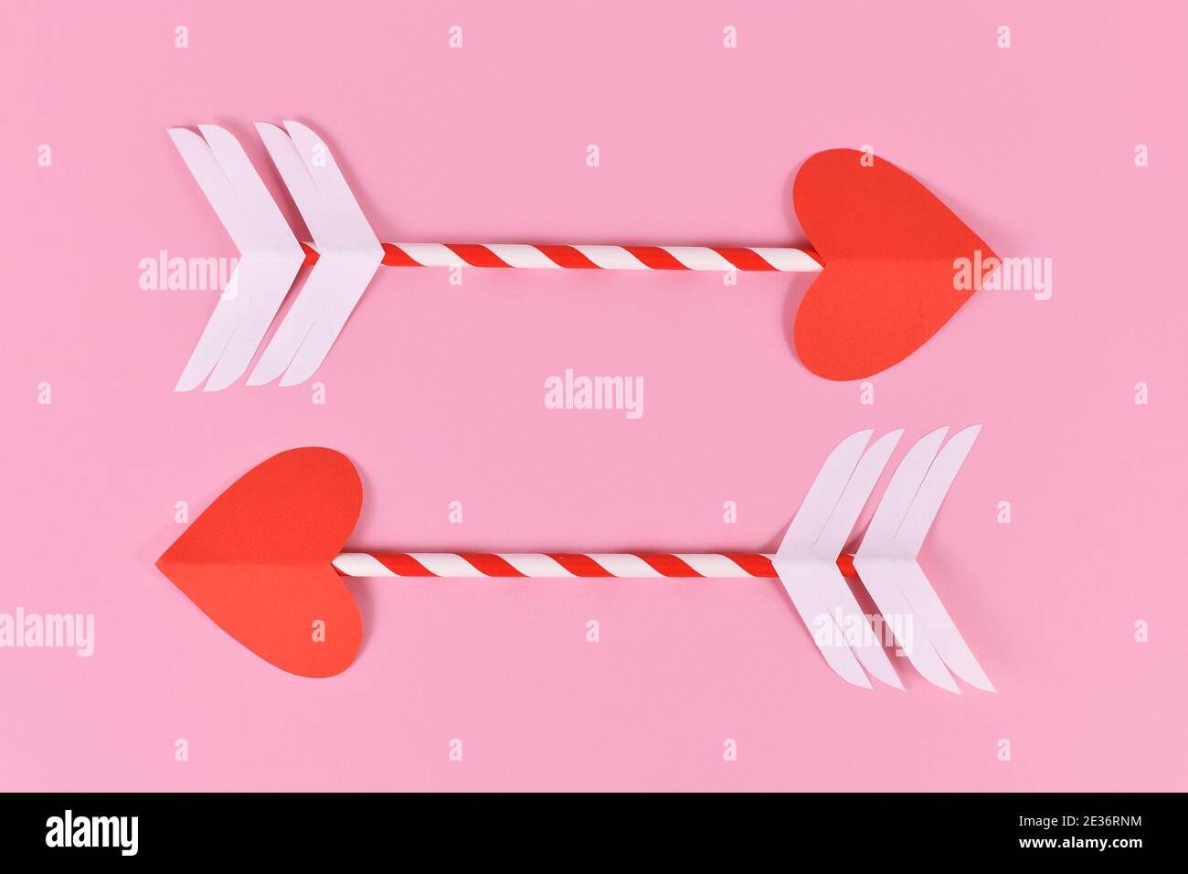 Due cupide freccia d'amore con punta a forma di cuore in carta su sfondo rosa Foto Stock