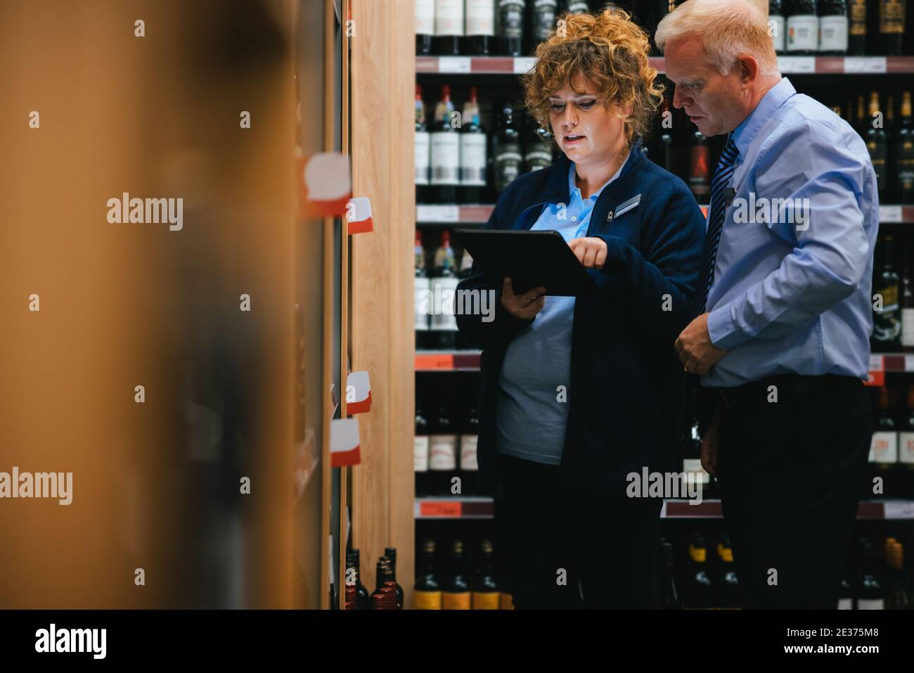 Liquori addetti al negozio che prendono a magazzino bottiglie di vino. Impiegati di supermercati di sesso maschile e femminile con tablet digitale che prende inventario di bottiglie di liquori. Foto Stock