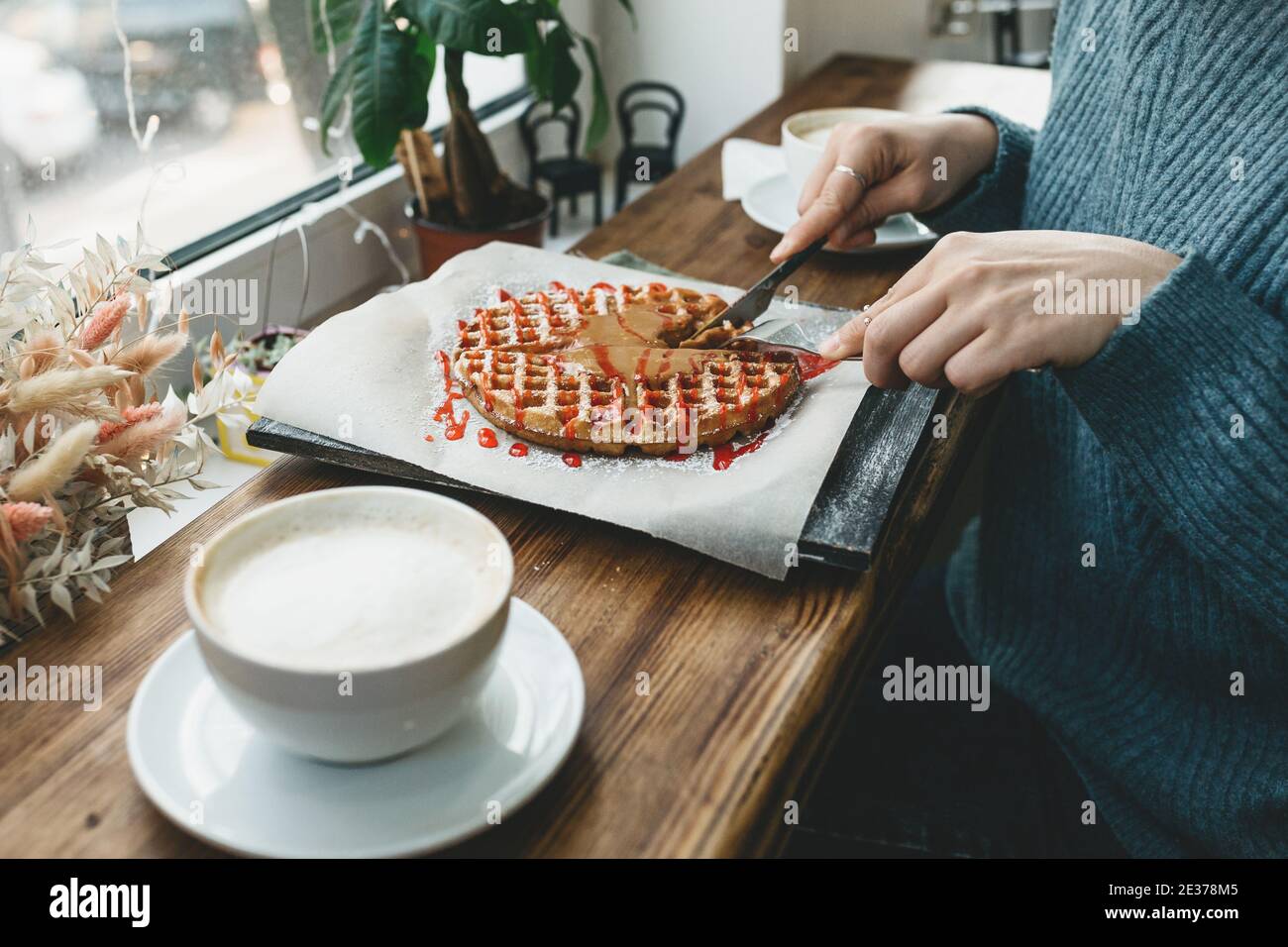 La ragazza taglia un waffle con cioccolato e sciroppo di frutta e sta per mangiare. Foto Stock