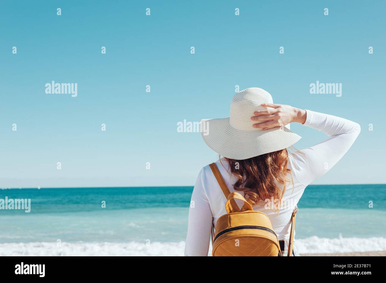 donna rossa che indossa un cappello e uno zaino giallo su una spiaggia mediterranea turchese Foto Stock