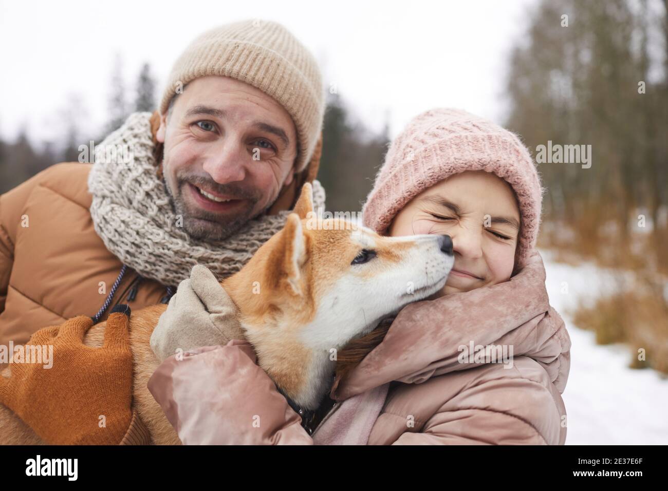 Primo piano ritratto di felice padre e ragazza che gioca con cane mentre si gode camminare all'aperto insieme nella foresta invernale Foto Stock