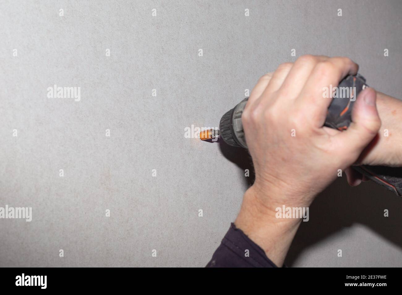 Un uomo usa un cacciavite per avvitare una vite in un muro a secco. Ristrutturazione della casa, rivestimento delle pareti. Foto Stock