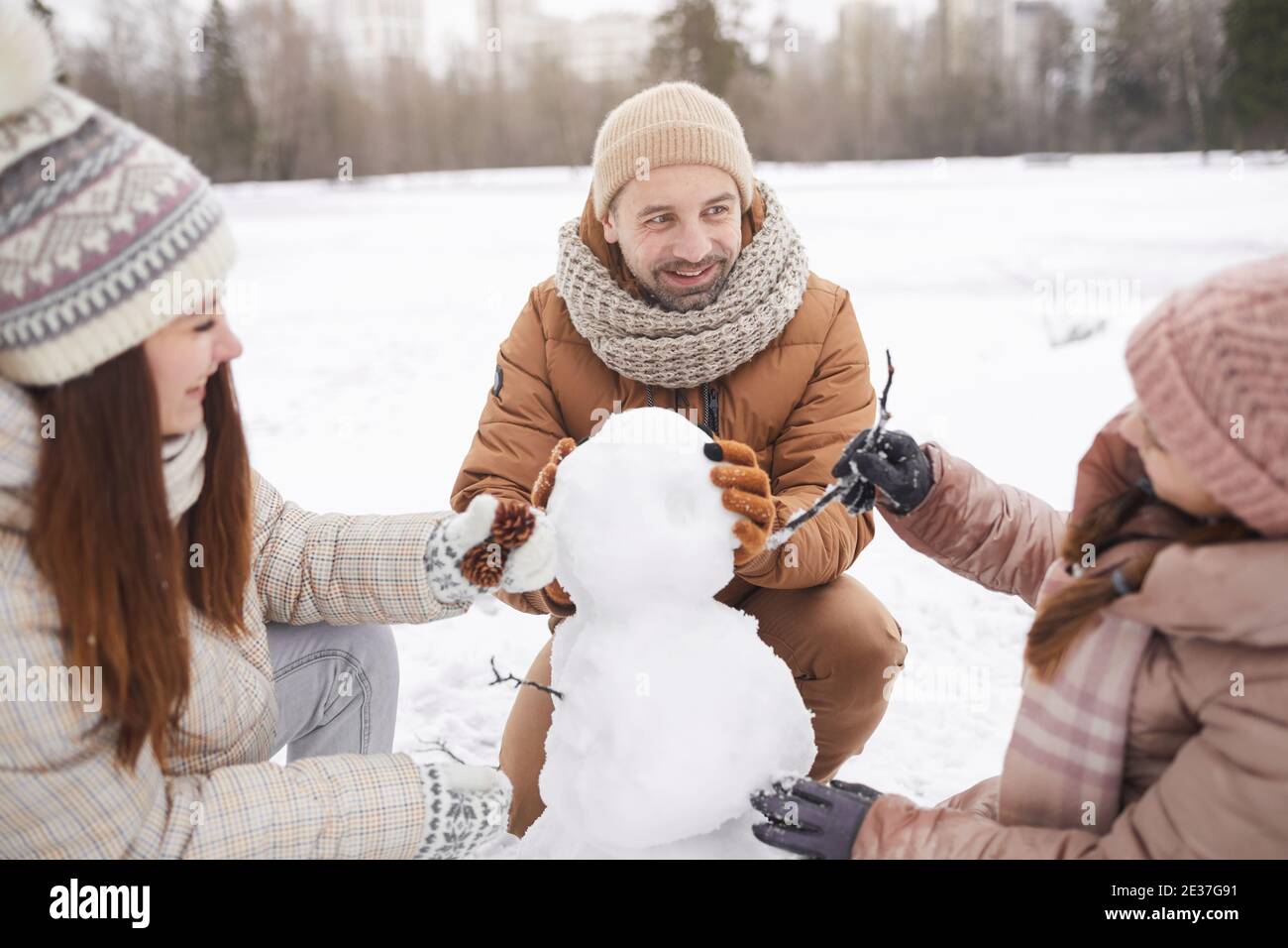 Ritratto di una famiglia felice che costruisce un pupazzo di neve insieme mentre si godono le vacanze invernali all'aperto, concentrarsi sul sorriso uomo maturo in primo piano Foto Stock