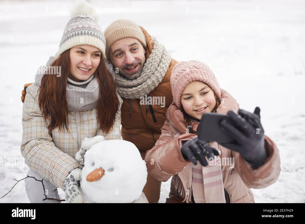 Ritratto ad alto angolo di una famiglia felice scattando foto selfie all'aperto mentre costruiamo insieme un pupazzo di neve e godendo la vacanza invernale Foto Stock