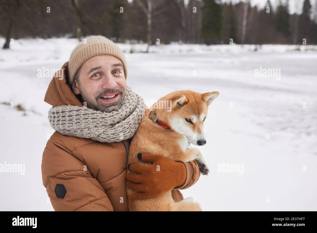 Vita in su ritratto di uomo sorridente maturo che tiene il cane e guardando la macchina fotografica mentre si gode la passeggiata nella foresta invernale, copia spazio Foto Stock