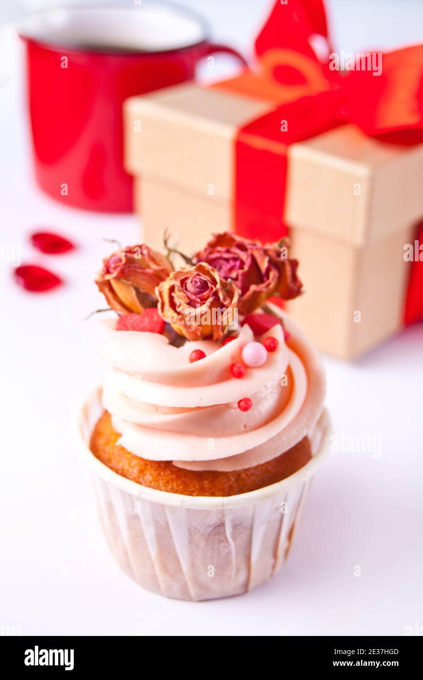 Crema di formaggio a base di cupcake di San Valentino decorata con fiori di rosa secchi, tazza di caffè e scatola regalo sullo sfondo Foto Stock