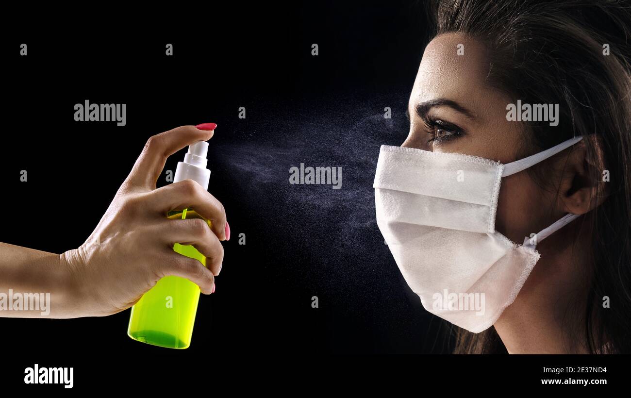 Ritratto concettuale di una donna che indossa una maschera igienica e che guarda allo spray antibatterico Foto Stock