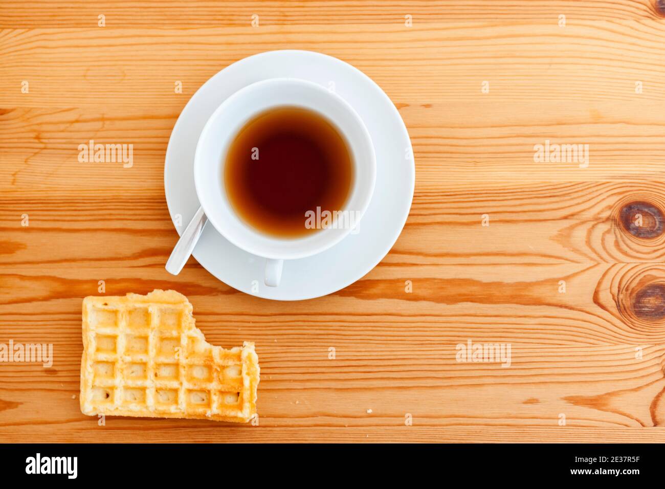 Tavolo in legno con tazza bianca con piatto e cucchiaio e waffle giacenti con punto di puntura nella vista dall'alto. Foto Stock