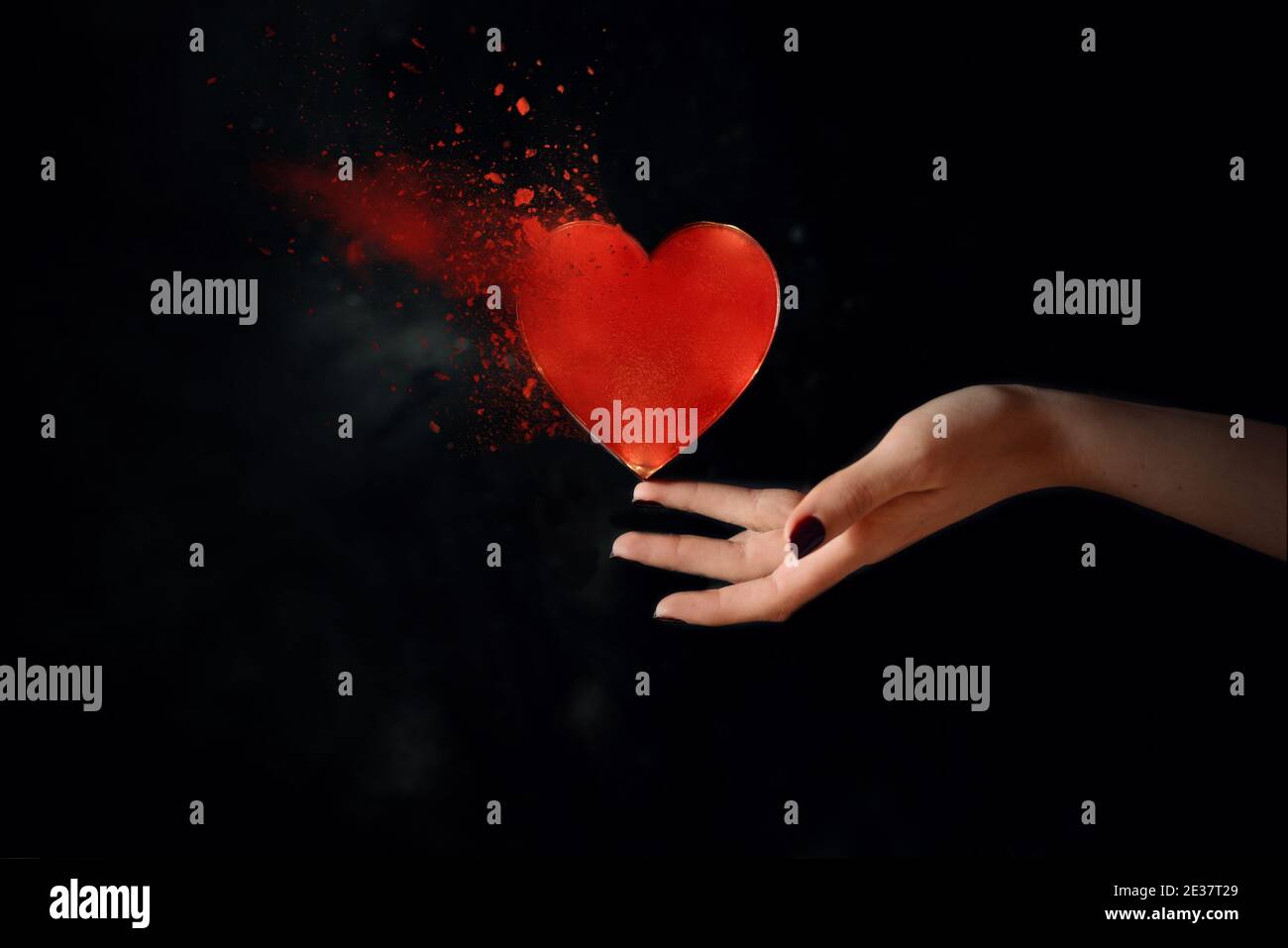 Donna mano equilibrando cuore rotto con polvere ed esplosione Foto Stock