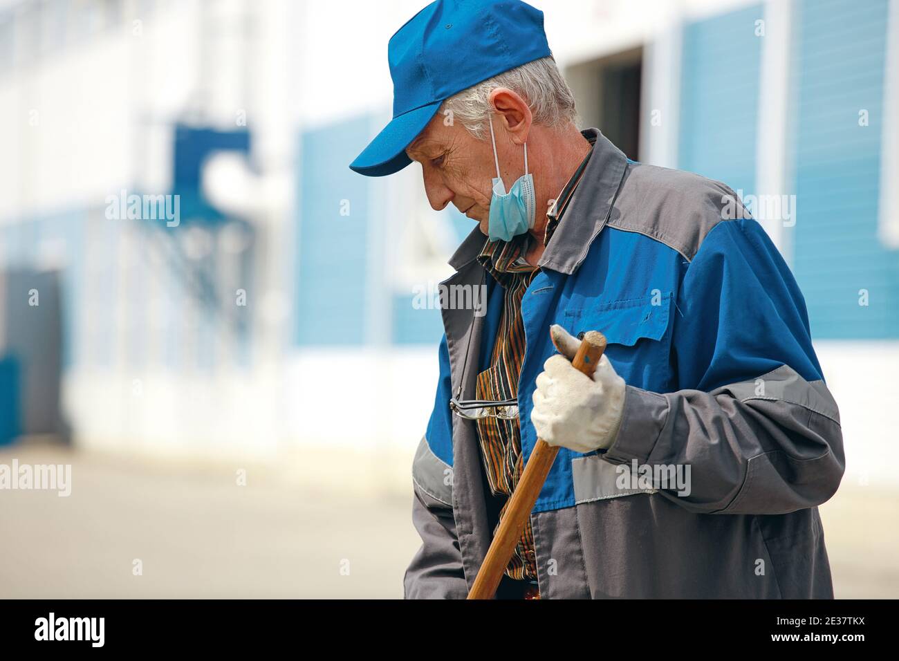 Si tratta di un anziano gianitore con una scopa in una maschera medica sulla strada che spazzano il territorio. Foto Stock