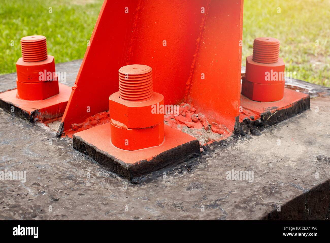 Il supporto in metallo rosso è imbullonato alla base in calcestruzzo con bulloni grandi. Fissaggio a terra di una torre o di una torre. Foto Stock